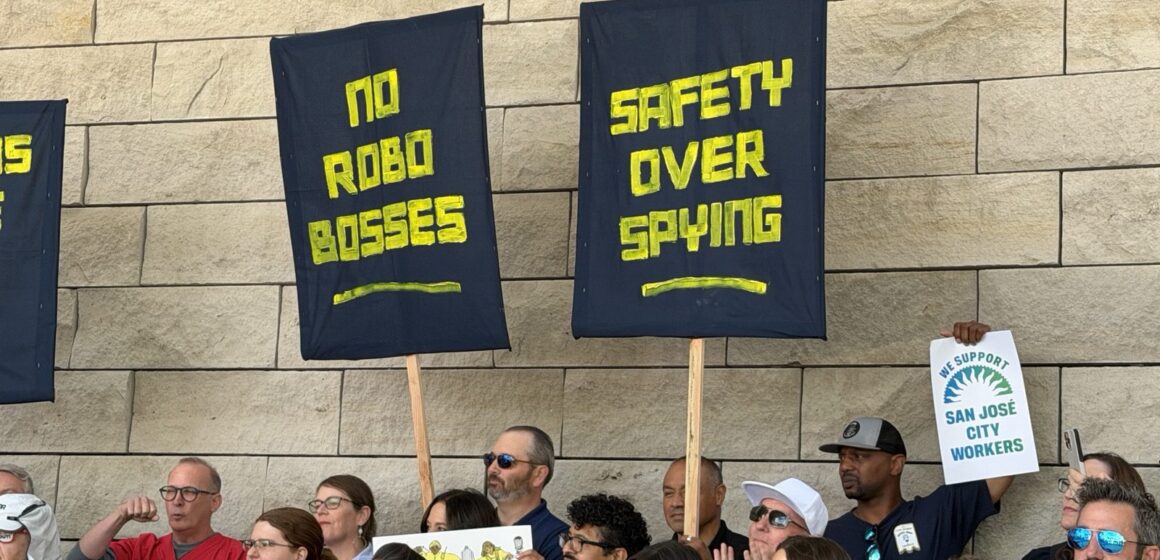 No robo bosses People’s Tech Coalition Workers hold up signs in front of a stone wall.