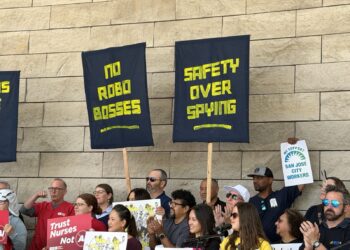 No robo bosses People’s Tech Coalition Workers hold up signs in front of a stone wall.