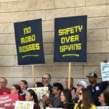 Workers hold up signs in front of a stone wall.