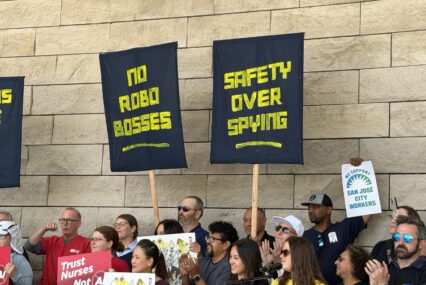 Workers hold up signs in front of a stone wall.