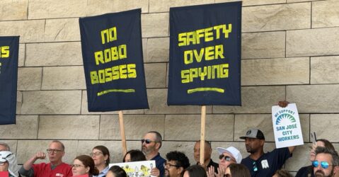 Workers hold up signs in front of a stone wall.