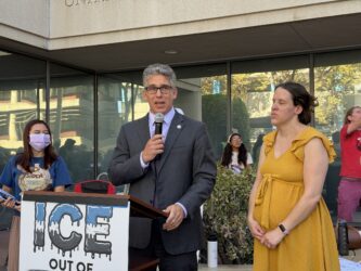 ICE federal court hearing A man speaking into a microphone at a podium outside in San Jose, California