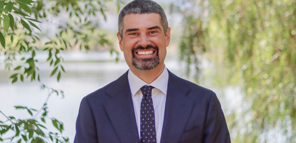 A man in a suit and tie standing outside smiling at the camera
