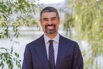 A man in a suit and tie standing outside smiling at the camera