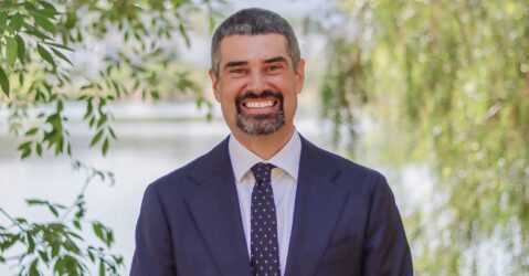 A man in a suit and tie standing outside smiling at the camera