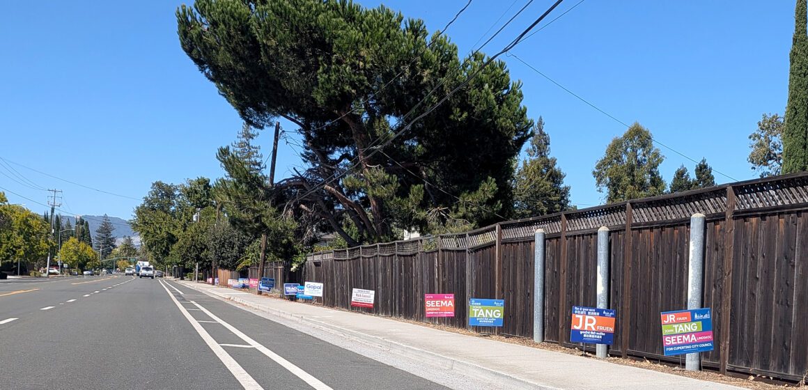 Campaign signs for a local election line a fence along a road in Cupertino, California