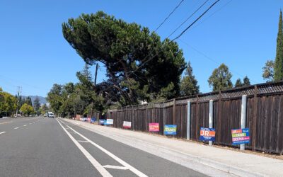 Campaign signs for a local election line a fence along a road in Cupertino, California