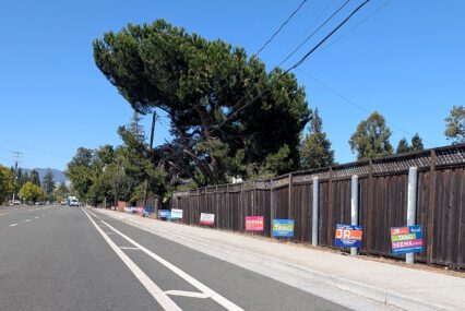 Campaign signs for a local election line a fence along a road in Cupertino, California