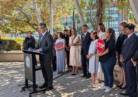 A man speaks at a podium outside with a row of people standing behind him in San Jose, California
