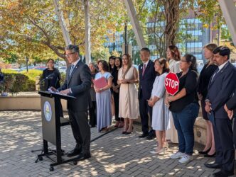 ICE Injunction 9/14/26 A man speaks at a podium outside with a row of people standing behind him in San Jose, California