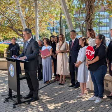 A man speaks at a podium outside with a row of people standing behind him in San Jose, California