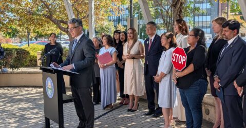A man speaks at a podium outside with a row of people standing behind him in San Jose, California
