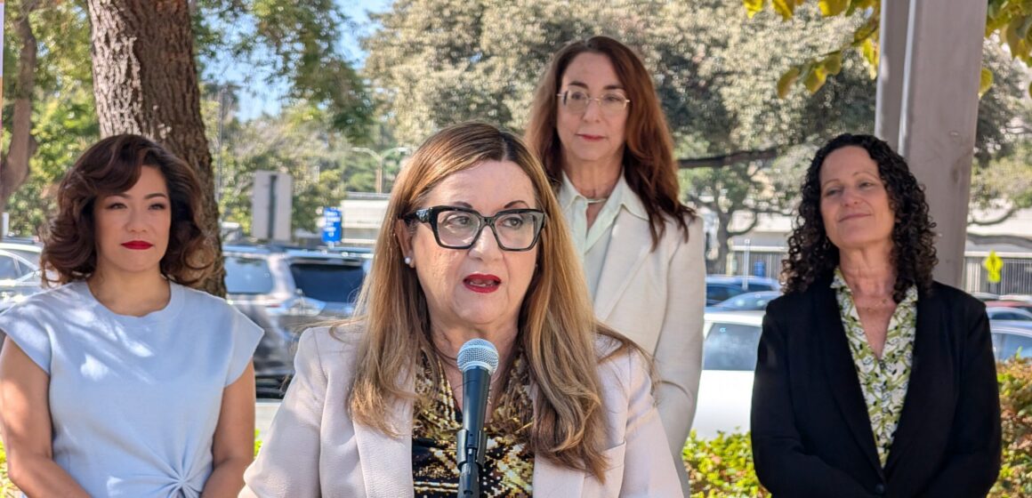 A woman speaking into a microphone, with other women standing behind her in San Jose, California