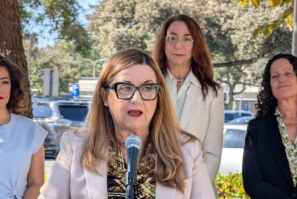 A woman speaking into a microphone, with other women standing behind her in San Jose, California