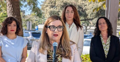 A woman speaking into a microphone, with other women standing behind her in San Jose, California