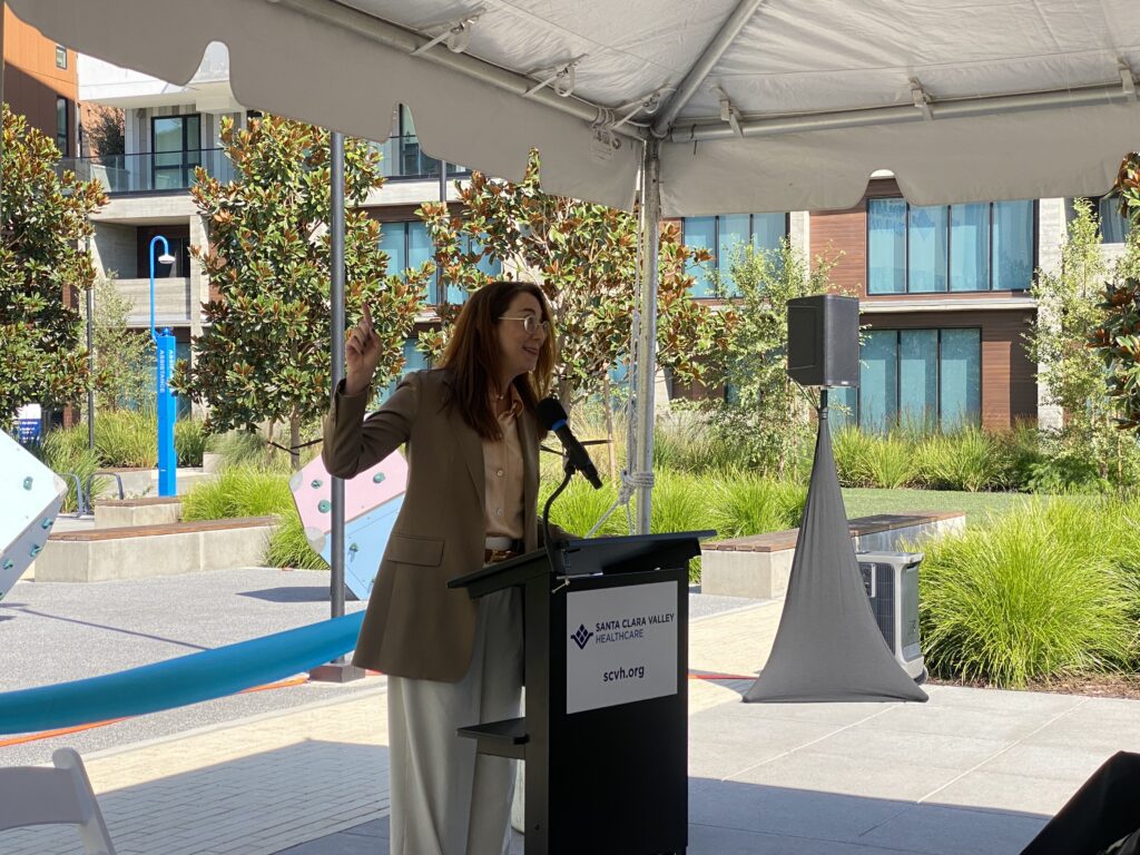 A woman speaking outside at a podium in San Jose, California