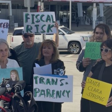 Kathy Watanabe Levi's press conference 2026 A woman speaking at a podium with people standing behind her holding signs in Santa Clara, California