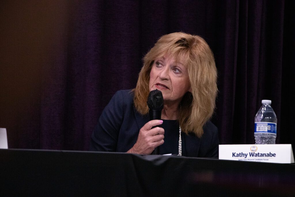 A woman holding a microphone at an election forum in Santa Clara, California