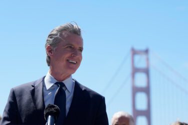 The governor of California standing in at a microphone, with the Golden Gate Bridge in the background