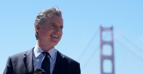 The governor of California standing in at a microphone, with the Golden Gate Bridge in the background