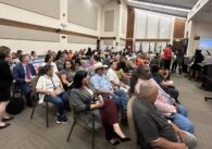crowd of people sitting down in a room looking forward.