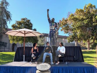 John Carlos -SJSU-2 resized Men sitting on a chair below his bronze statute