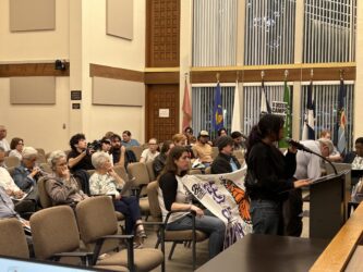 GILROY DC MORATORIUM EXT People sitting in chairs at a government meeting in Gilroy, California, with one speaker standing at the podium